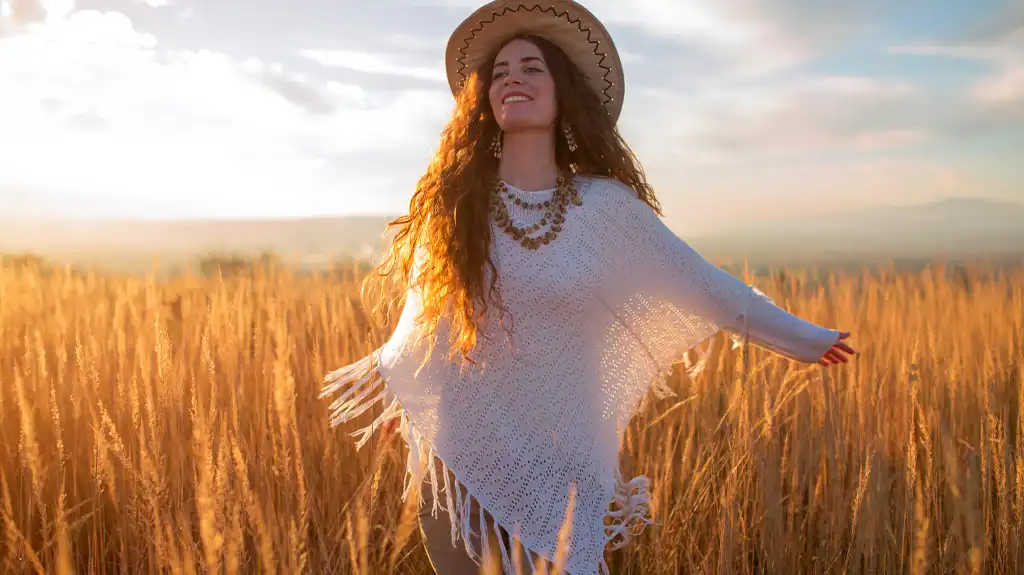 Women's poncho Christmas gifts young blonde woman with long hair, wearing a white poncho running in a wheat field